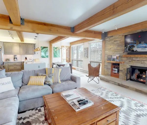 This image shows a cozy living room with a large gray sectional sofa, a fireplace under a wall-mounted TV, and a wooden coffee table.