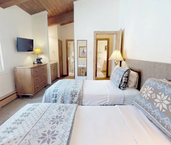 The image shows a cozy bedroom with two single beds adorned with patterned bedding, a dresser with a TV, and a mirror on the wall.