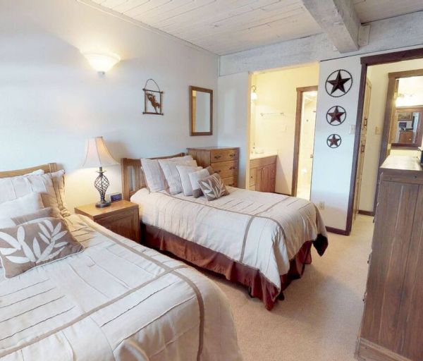 The image shows a cozy bedroom with two single beds, a dresser, wall decor featuring stars, a lamp, and a TV near an open door to another room.