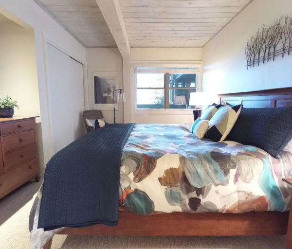 The image depicts a cozy bedroom with a large bed, wooden furniture, a TV, a window, and decorative items on the wall and dresser.