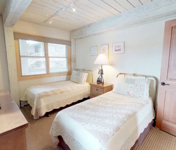 A cozy bedroom with two twin beds, a wooden dresser, a TV, a lamp, three pictures on the wall, and a window providing natural light.