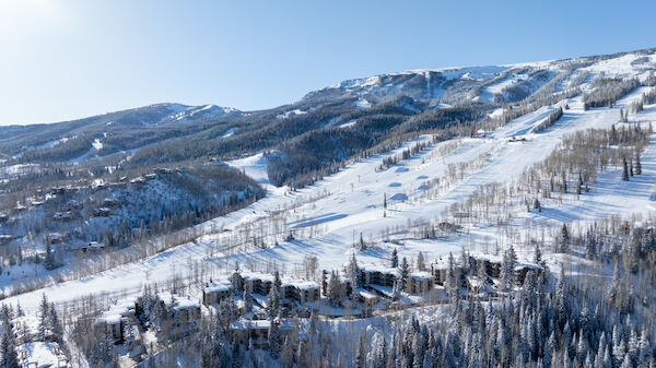 Asnowy mountain landscape with slopes, pine trees, and a clear blue sky, likely a ski area with chairlifts and trails.