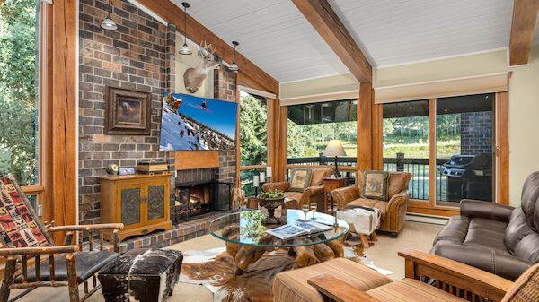 The image features a cozy living room with a mix of rustic decor, featuring a fireplace, large windows, and comfortable seating.