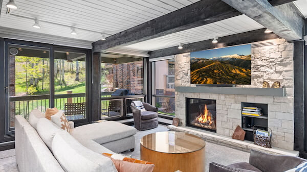 A cozy living room with a fireplace, large windows, couches, armchairs, and a coffee table, featuring a scenic landscape picture.