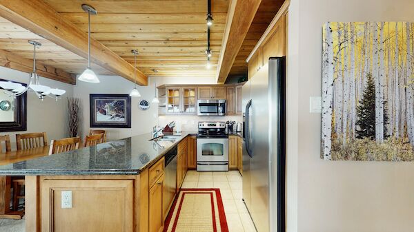 A modern kitchen and dining area with wooden accents, granite countertops, and stainless steel appliances, featuring a forest-themed painting.