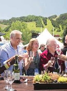 A group of five people toast while enjoying drinks outdoors against a mountainous backdrop, celebrating together in a lively atmosphere.