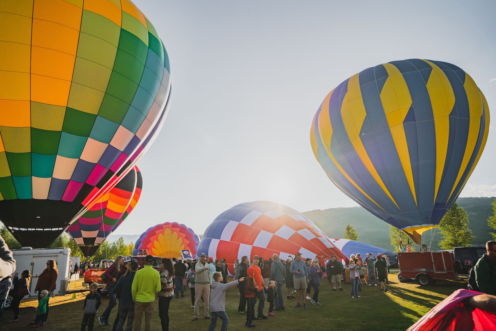 The image shows colorful hot air balloons at an outdoor event, with people gathered around enjoying the vibrant scene.