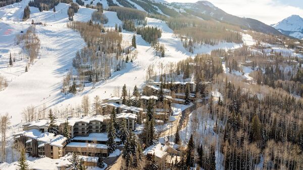 The image shows a snowy mountain landscape with ski slopes, trees, and a cluster of buildings below, creating a scenic winter scene.